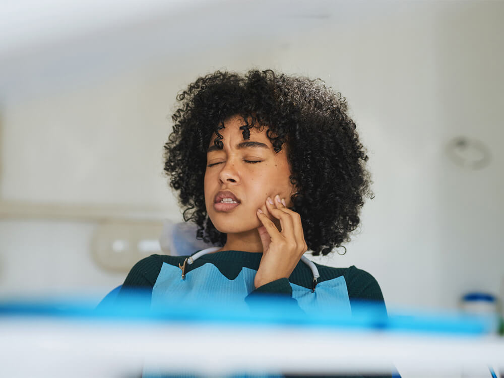 Female patient holding her jaw and wincing in pain at Urgent Dental in Matthews, NC.